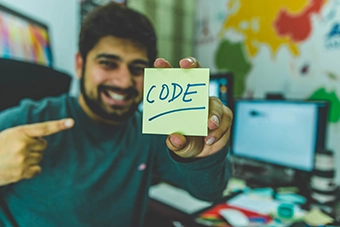 programmer smiling with code written on sticky note