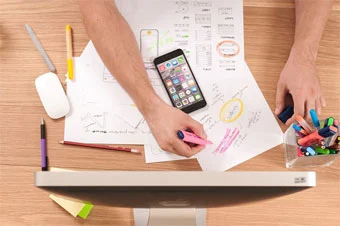 man sketching mobile wireframe on paper at a desk